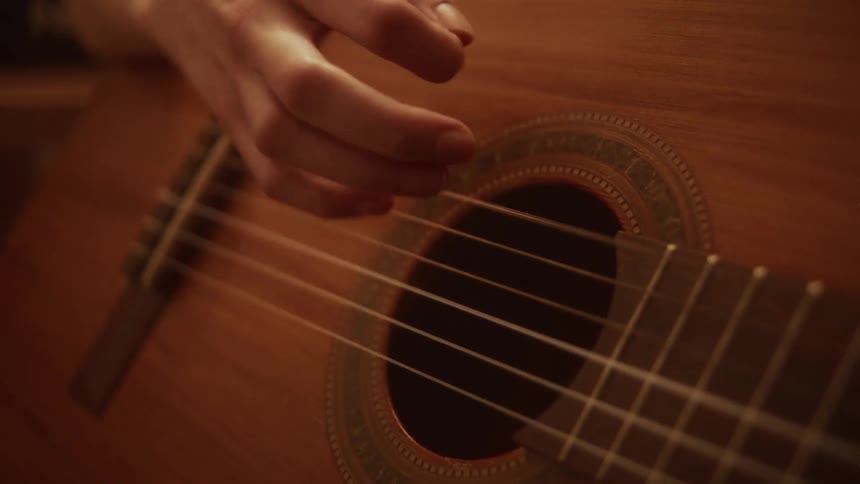 Close-up shot of a hand energetically strumming the strings of a classical acoustic guitar in warm lighting