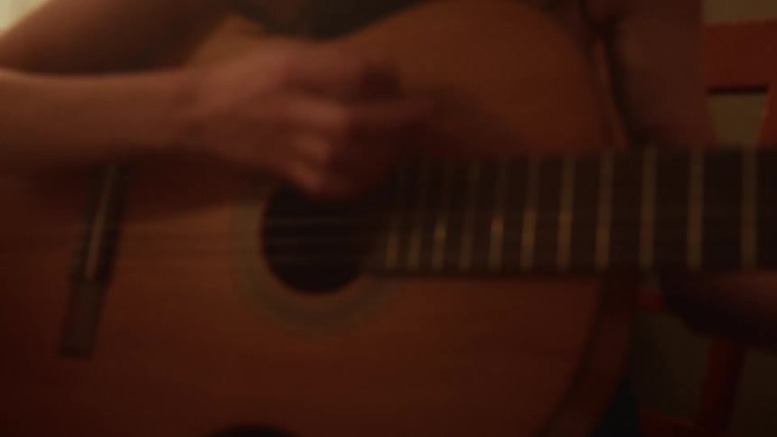 A young woman passionately plays her acoustic guitar and sings in a cozy, softly lit room at home