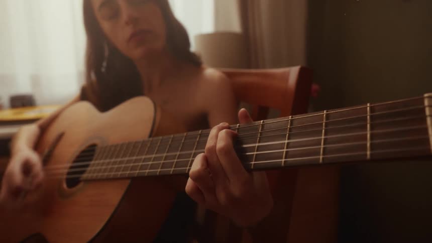 Dreamy close-up of a talented woman singing and playing the guitar at home by a sunny window