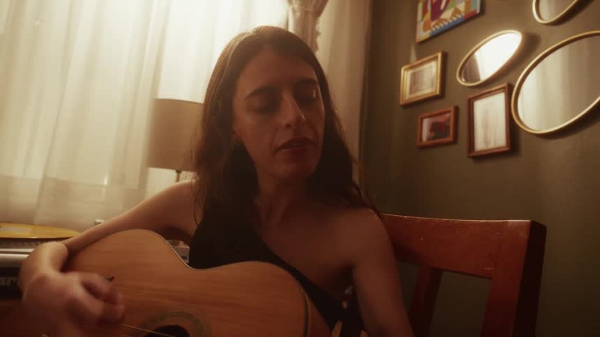 An intimate slow-motion shot captures a woman lost in song as she plays the acoustic guitar in her room