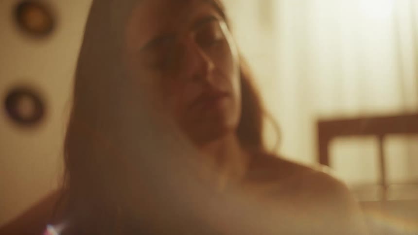 An emotional woman with long hair plays an acoustic guitar in a warmly lit room, with the camera slowly tilting up to her face