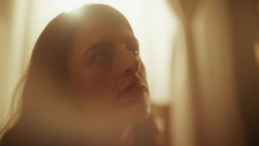 A contemplative woman's face is softly illuminated by a warm, hazy light, creating a pensive and dreamlike atmosphere