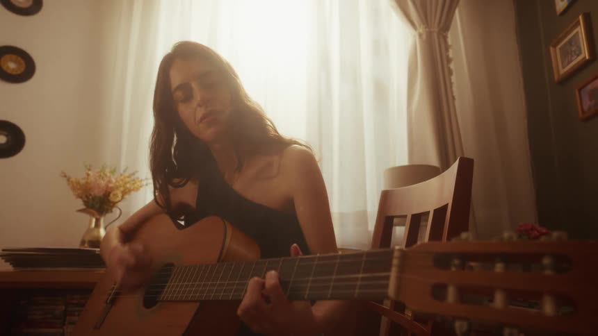 A young woman plays the acoustic guitar with feeling in a room filled with warm, golden light