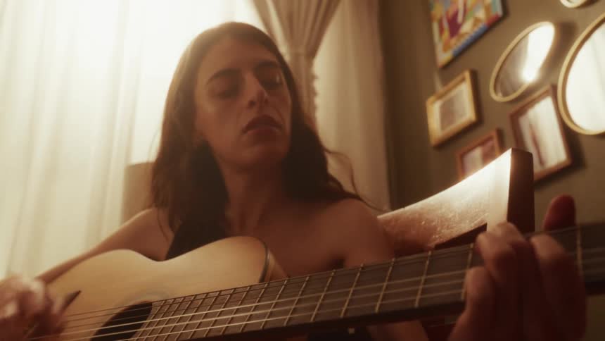 Low angle shot of a focused musician playing an acoustic guitar in a warm, softly lit room