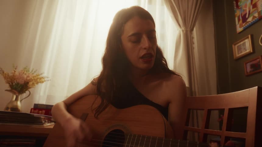 A passionate female musician sings and plays an acoustic guitar in her sun-drenched, cozy room