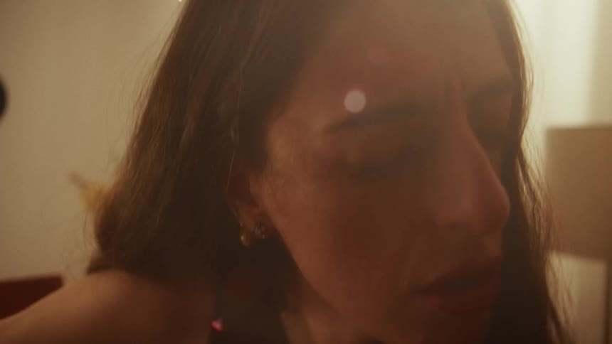 A hazy and emotional close-up of a woman with her eyes closed, singing softly in a warmly lit room