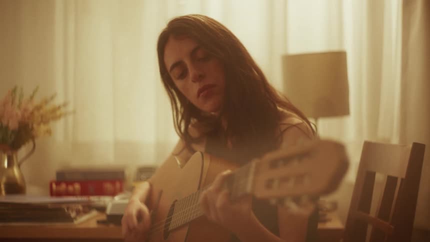 A focused young woman passionately plays an acoustic guitar in a softly lit room