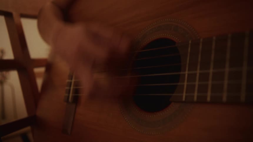 Intimate close-up of a musician's hands playing and strumming an acoustic guitar in a dimly lit, warm room
