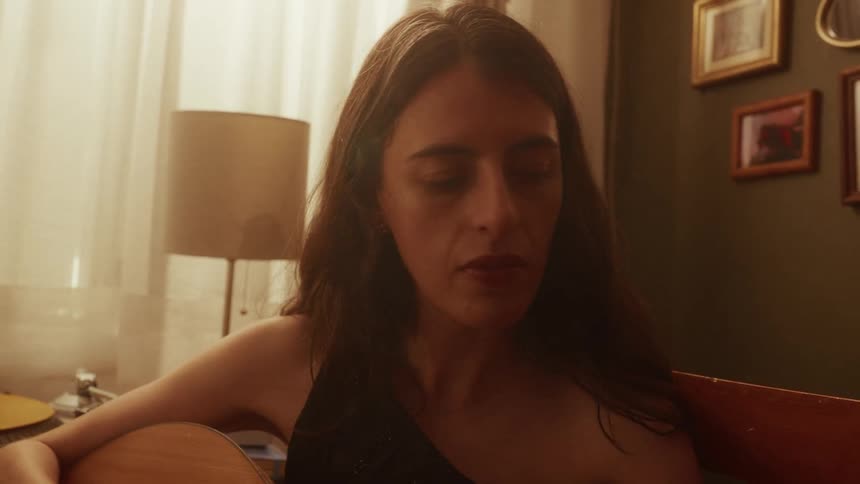 Close-up of a contemplative woman holding an acoustic guitar in her warmly lit, vintage-style room