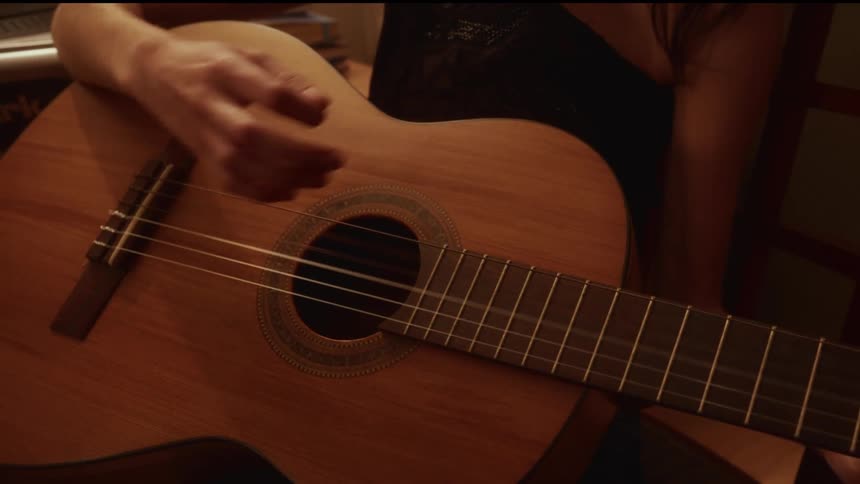 Close-up of a musician's hand strumming the strings of an acoustic guitar in a dimly lit room