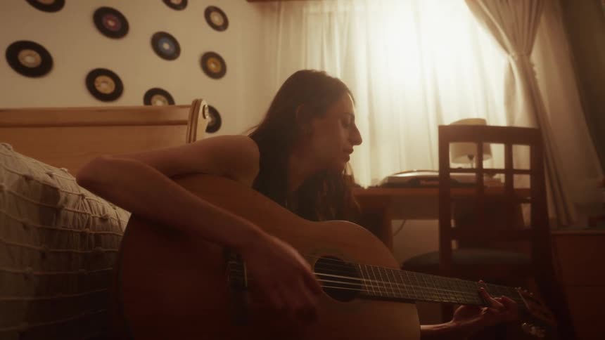 A passionate young woman plays an acoustic guitar and sings in her warmly lit bedroom