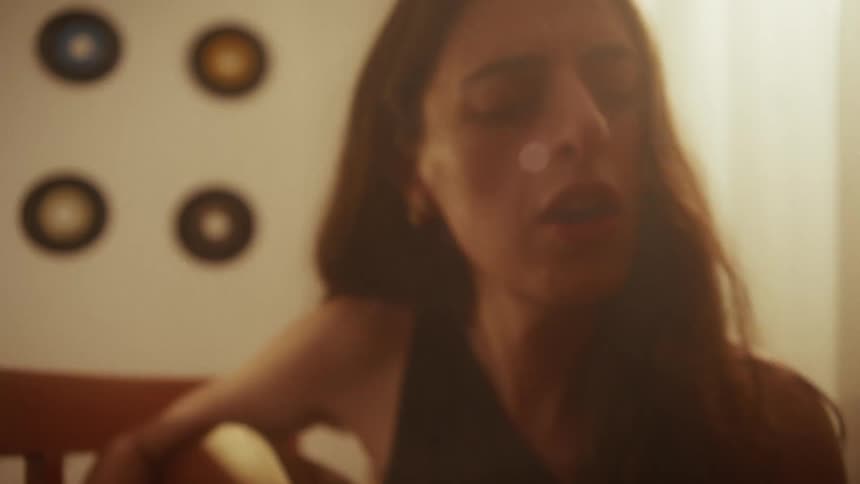 An emotional musician plays her acoustic guitar and sings a heartfelt song in a warm, hazy room