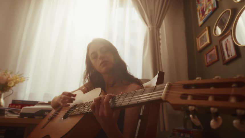 Low angle shot of a woman passionately playing an acoustic guitar in her sun-drenched room