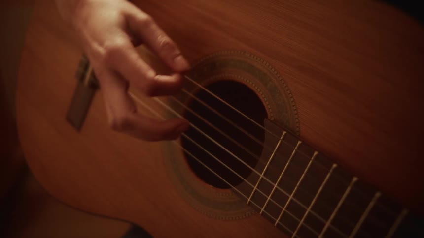 A close-up shot shows a musician's hand strumming the strings of a classical acoustic guitar