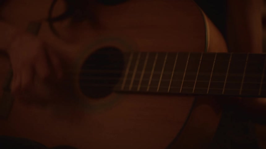 Close-up of a musician's hands playing chords and strumming an acoustic guitar in a warmly lit room