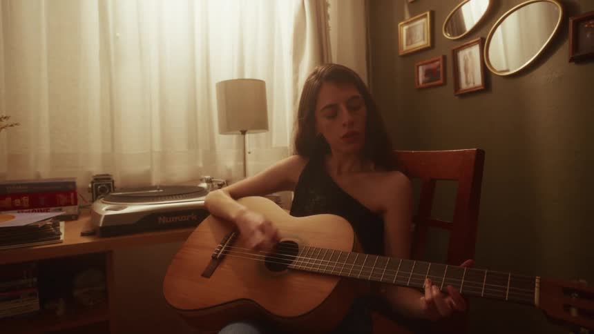 A talented young woman plays a heartfelt melody on her acoustic guitar in a warmly lit, vintage-style room