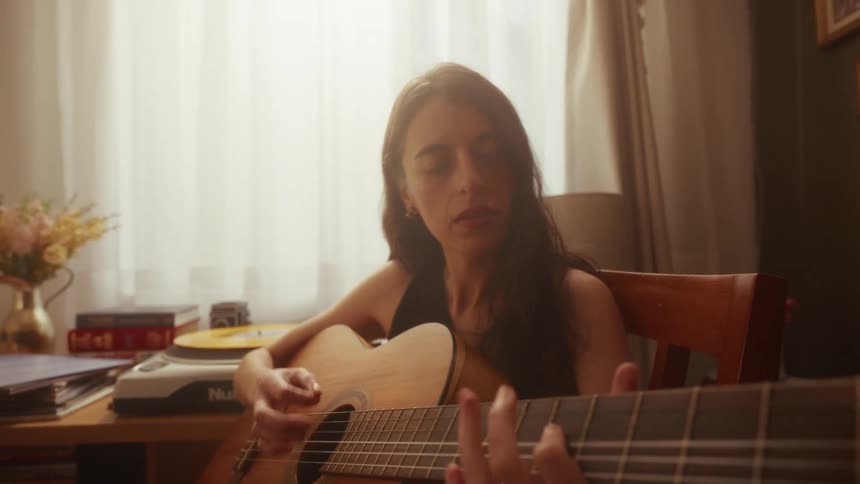 A close-up shot of a young woman passionately playing the acoustic guitar in a warm, sunlit room