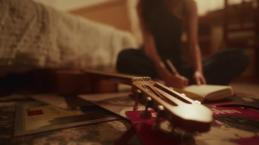 An inspired musician writes in a journal on the floor of a cozy bedroom, with an acoustic guitar and vinyl records in the foreground