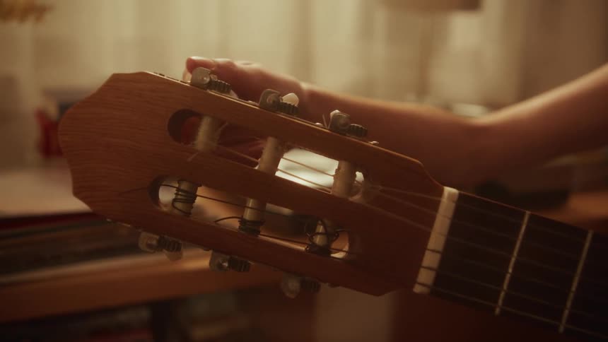A close-up of a hand delicately turning the tuning pegs on the headstock of a classical guitar