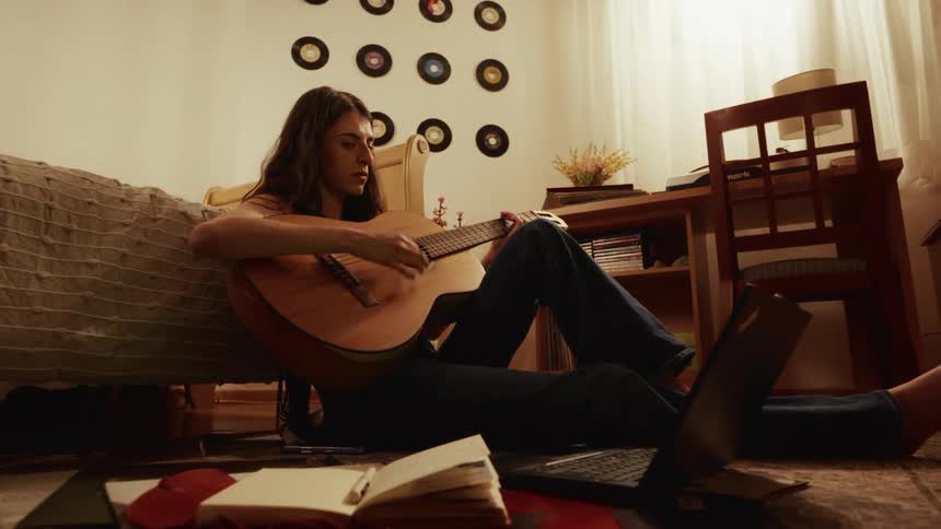 A creative woman plays her acoustic guitar while writing songs in her cozy, retro-style bedroom