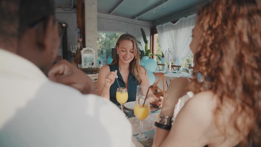 A beautiful woman smiles and chats with her friends during a celebratory brunch at a sunlit restaurant