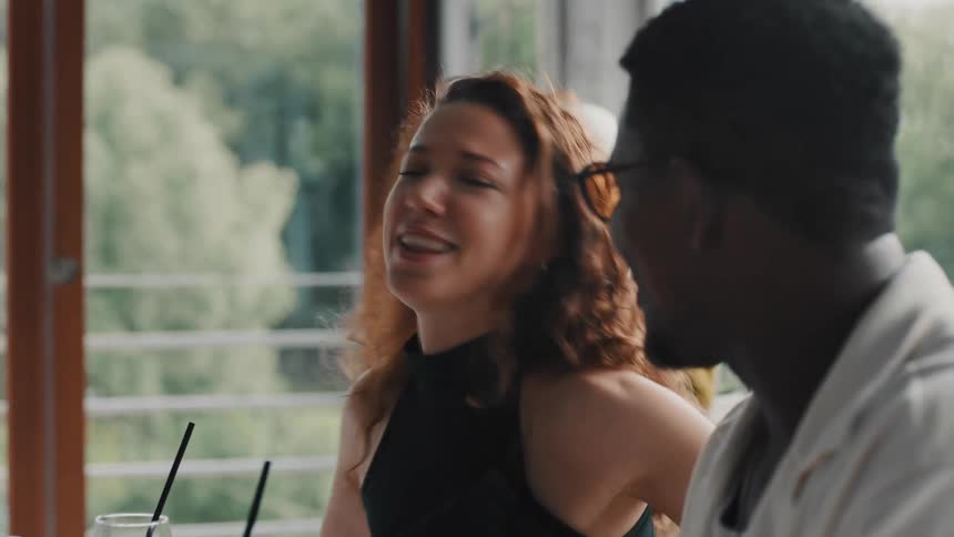 A young woman with curly hair animatedly talks to a man while sitting in a restaurant during the day