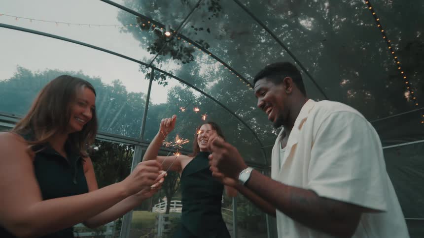 A diverse group of friends celebrate with sparklers, laughing and dancing in slow motion at an outdoor evening party