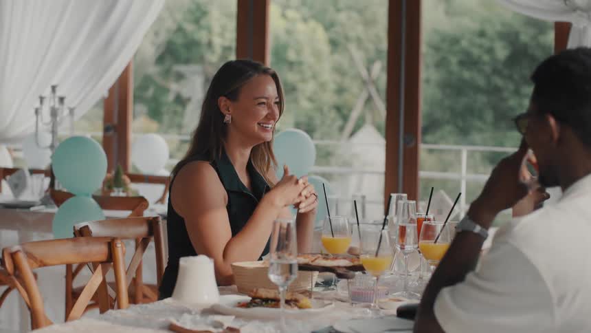 A happy woman laughs and gives two thumbs up while having a conversation at a celebratory brunch in a bright restaurant