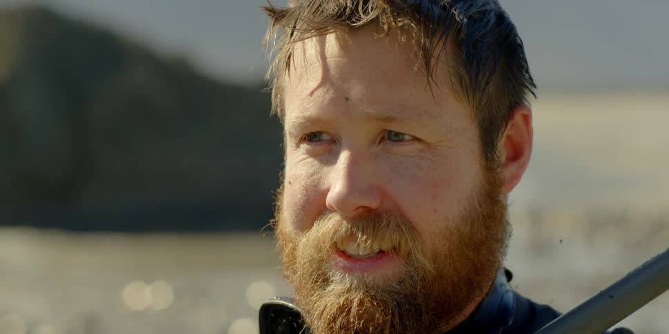 A bearded man smiles and looks around