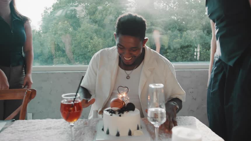 Joyful diverse friends surprise a man with a birthday cake, hugging and dancing around him as he laughs in slow motion