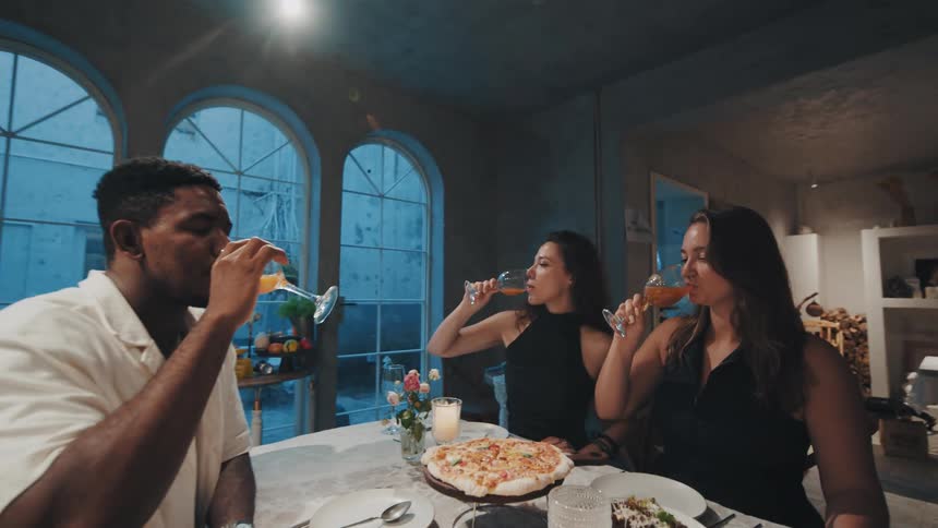 A diverse group of smiling friends enjoys a celebratory dinner, toasting with glasses in slow motion