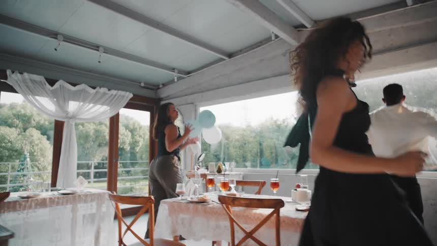 A diverse group of happy friends dance energetically in slow motion during a daytime celebration in a brightly lit restaurant