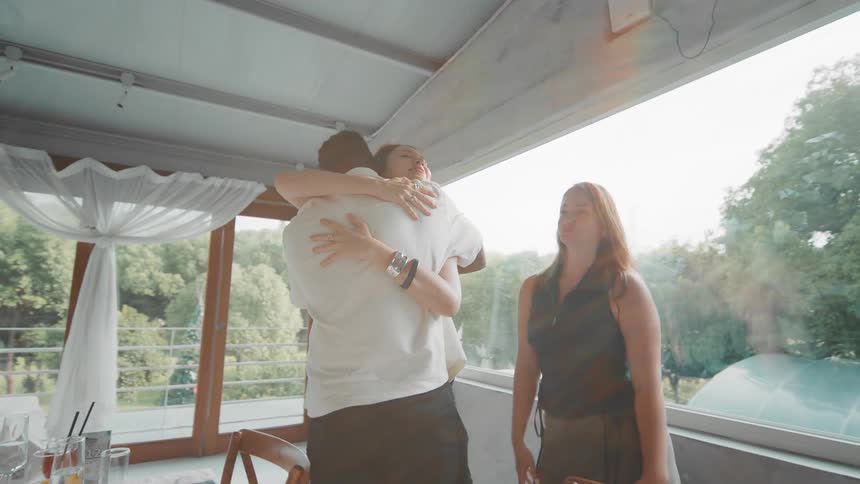 A happy group of diverse friends hug and dance together in a sunlit restaurant, celebrating their reunion