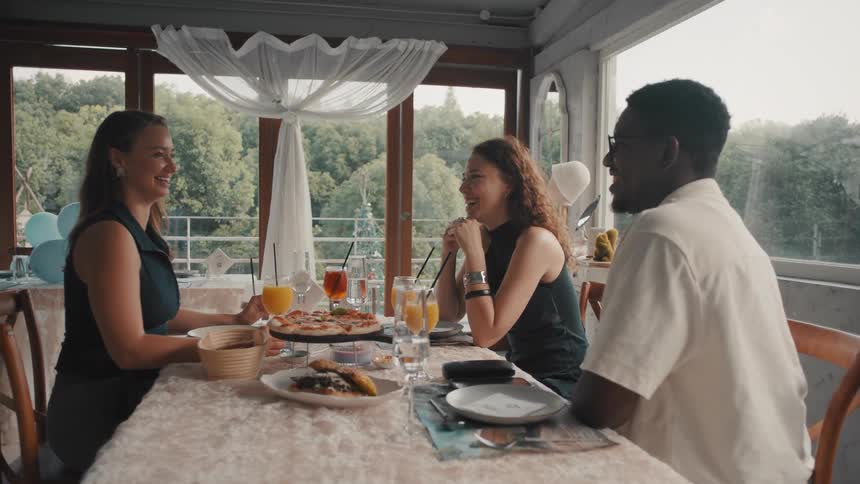 A diverse group of friends laugh and enjoy a meal together at a bright and beautiful restaurant