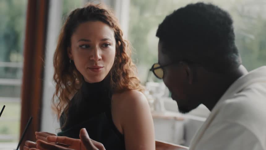 Slow motion close up of a diverse couple having a conversation while enjoying a meal at a sunlit cafe