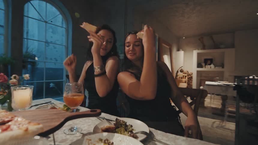 Two female friends groove to the music while enjoying pizza at a stylish dinner party