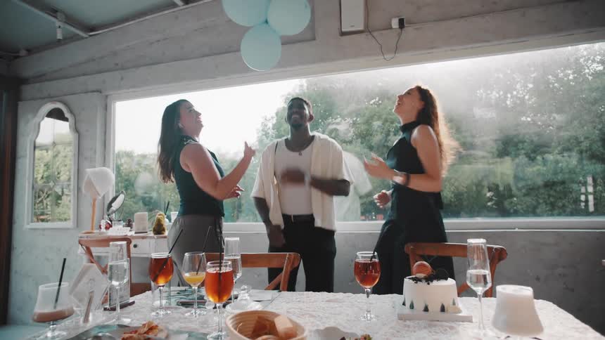 Slow motion shot of diverse friends laughing and dancing with balloons at a birthday party in a sunlit restaurant