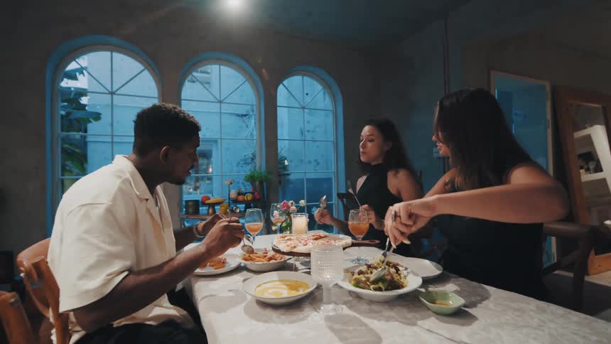 A diverse group of friends enjoy a cozy dinner together, sharing pizza, salad, and conversation in a stylish restaurant