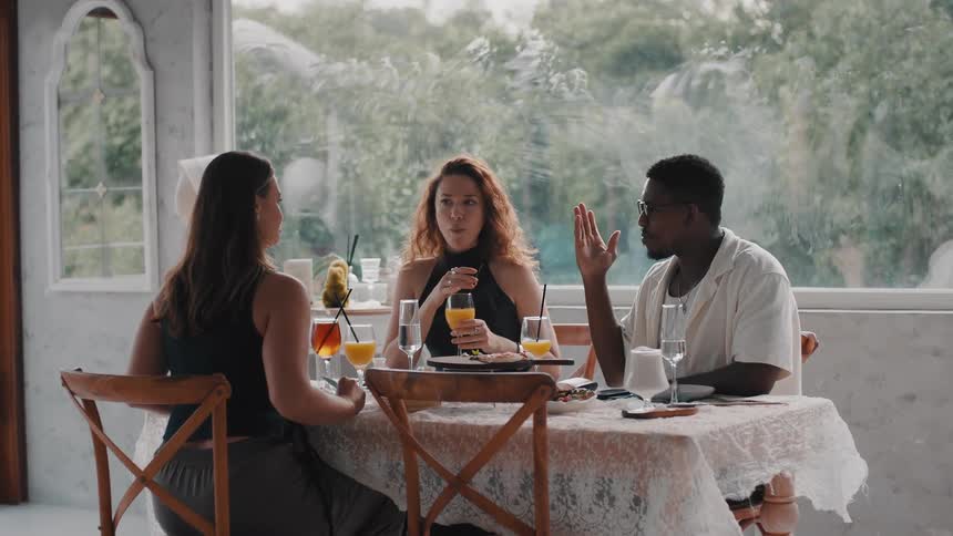 A diverse group of friends enjoys a lively conversation over brunch at a chic, sunlit restaurant