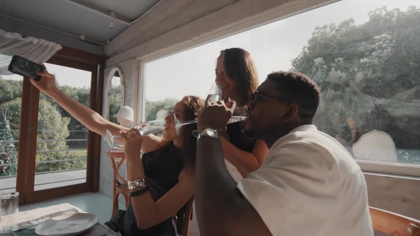 A joyous group of multiracial friends takes a selfie while drinking champagne and celebrating at a restaurant
