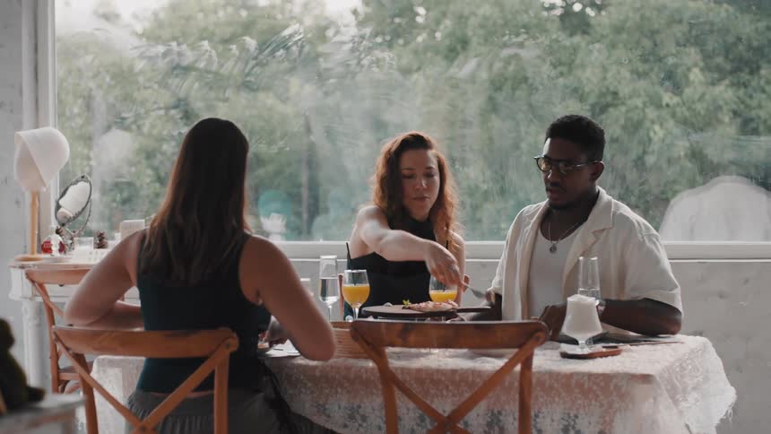 A diverse group of three friends enjoys a conversation while having a meal together at a stylish cafe