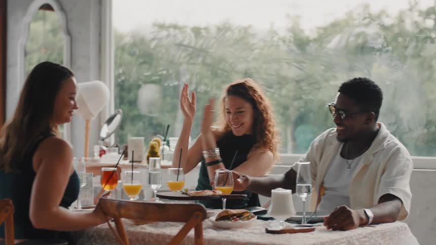 A diverse group of friends celebrates joyfully in a bright restaurant, laughing and giving high-fives in slow motion
