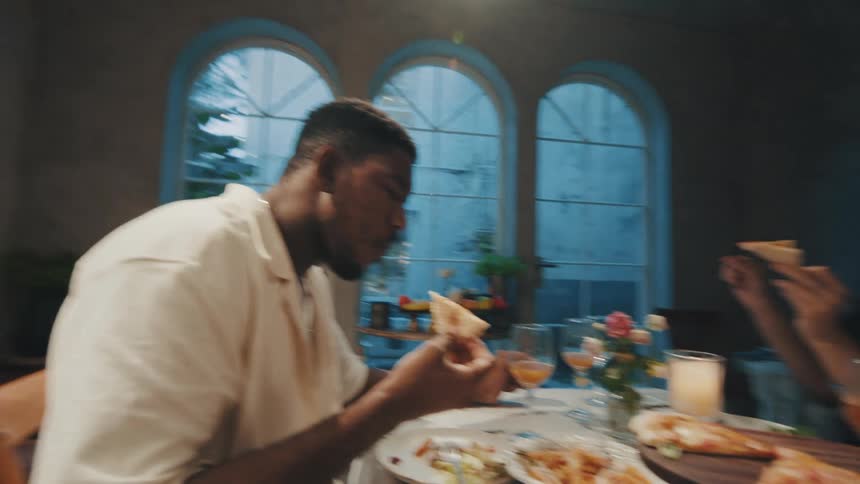 A slow pan reveals a diverse group of friends enjoying a delicious dinner party together in an elegant dining room at dusk