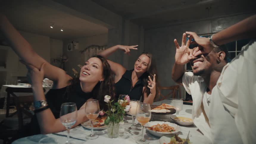 A group of diverse friends have fun taking silly selfies while enjoying a dinner party at home