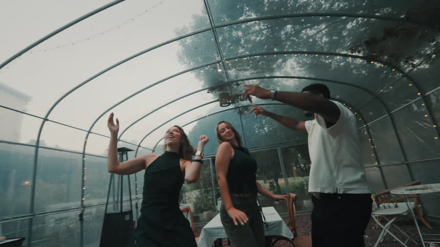 A group of diverse young friends dance together with smiles and joy at a party inside a greenhouse in slow motion