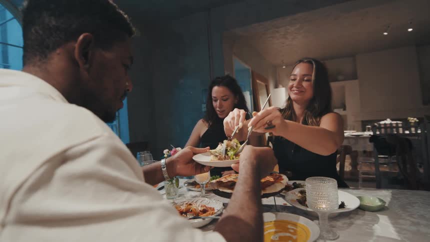 A diverse group of happy friends share food and enjoy conversation during a dinner party at a modern home