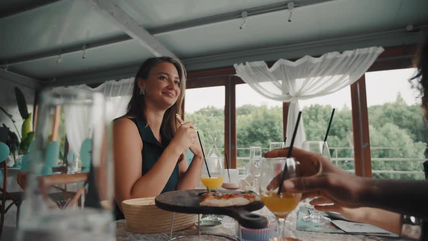 A diverse group of happy friends toast with glasses of juice in slow motion while enjoying a celebratory meal at a beautiful restaurant
