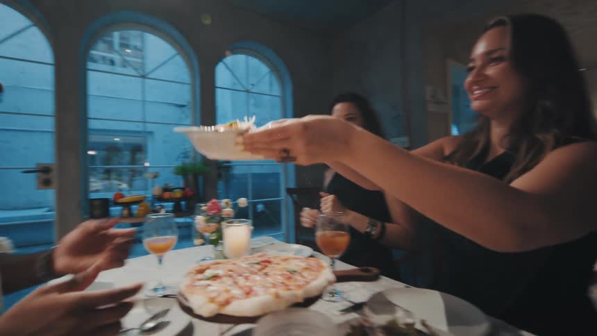 Happy diverse friends share delicious Italian food at a dinner party, passing dishes of pasta and salad in slow motion