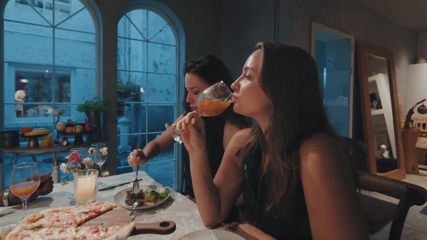 A group of friends enjoys a relaxed dinner with pizza and drinks at a stylish restaurant in the evening