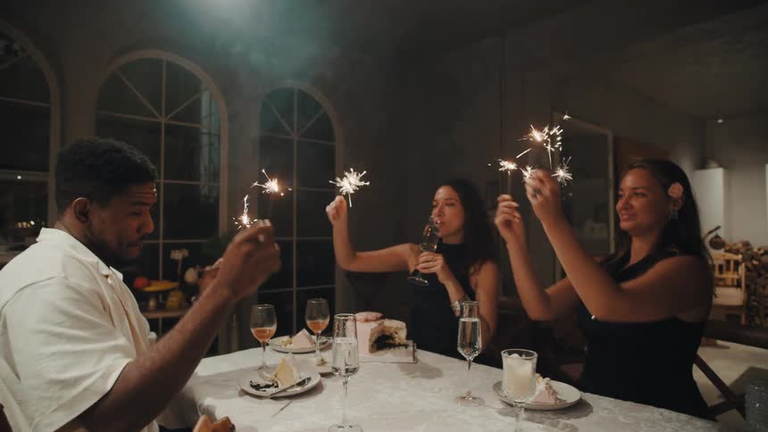 Diverse group of friends enjoy a festive birthday dinner, holding up sparkling sparklers in celebration